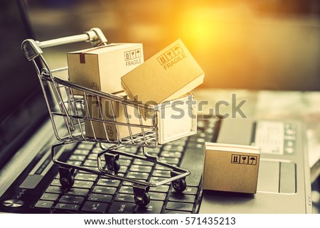 Small paper cartons or boxes in shopping cart with one falls outside on a laptop keyboard. Concept about online shopping that everybody can buy or purchase everything easily at hand just a few clicks.
