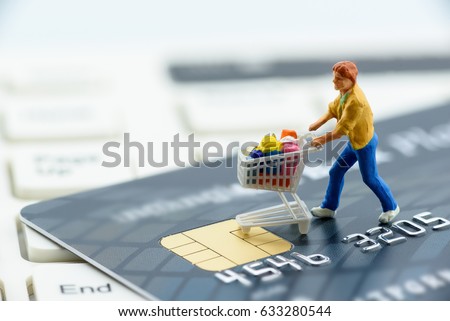 Miniature figurine : a shopper pushes a shopping cart on a smart credit card and a keyboard. Concept of brick and mortar stores nowadays face with increased competition from internet online ecommerce.