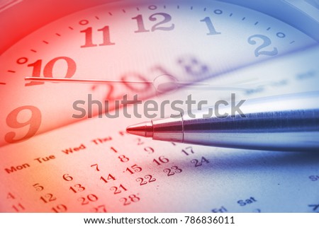 Calendar planner for year 2018 concept : Blue metal pen on a paper desk calendar with analog clock and a clock hand, implies the passing of time, planning or making time schedule for future project.