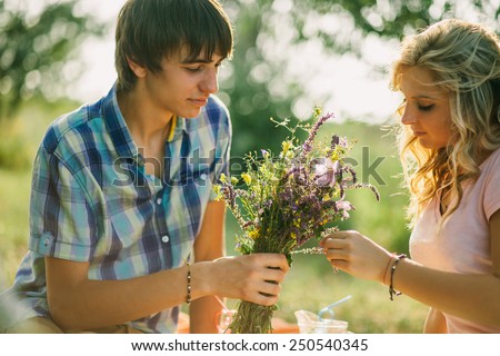 teenage couple dating on picnic in green park with flowers in country style