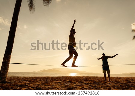 teenagers balance slackline on sunrise beach silhouette