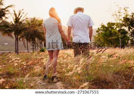 honeymoon couple vacation in meadow hands together back view at sunset