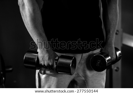 bodybuilder guy in gym with fitness dumbbells hands close up. Black and white