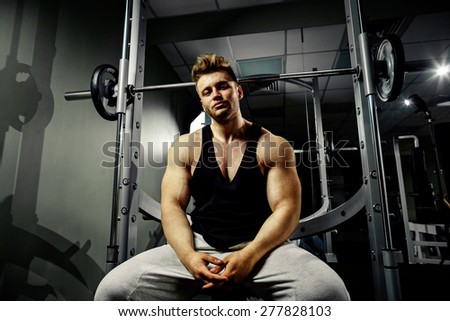 strong bodybuilder handsome athlete in black tank top with high weights in gym