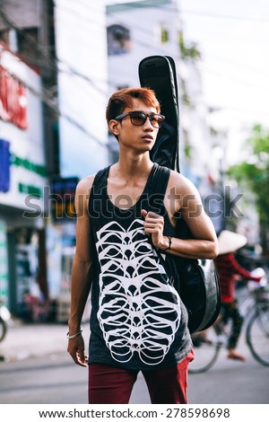 asian guitarist artist man in sunglasses walk on vietnamese street