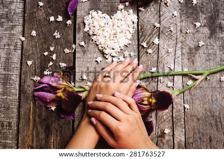 proposal wedding ring on hand close up with heart shape white lilac flowers and violet irises on vintage wood table top view