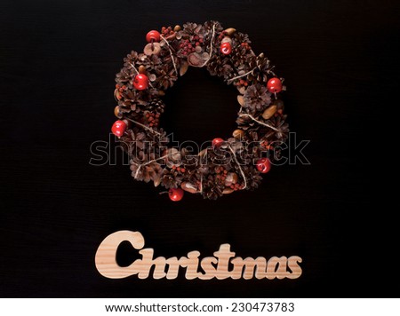 A festive christmas wreath and a christmas wooden writing on a black pine background.