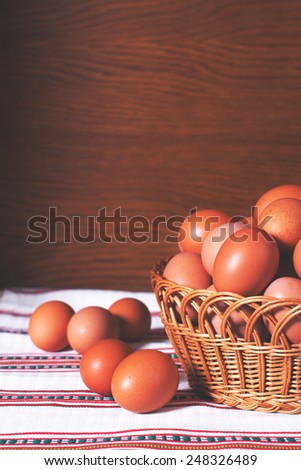 Hen eggs from a farm in a woven basket on a wooden background and a white ornamented towel. Vertical oriented. Easter, food, diet and nutrition stock image