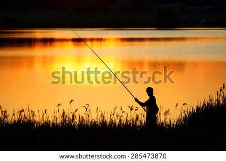 Fisherman fishing at dusk with a rod. Backlit silhouette of a fisherman