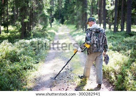 Treasure hunter with metal detector and shovel in forest