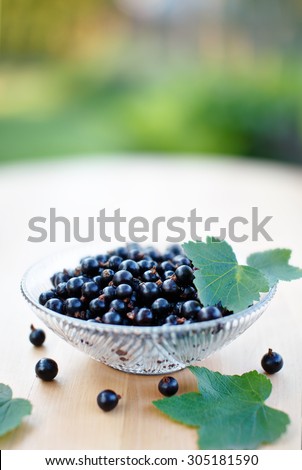 Ripe black currant berries in glass bowl on wooden table. Shallow depth of field