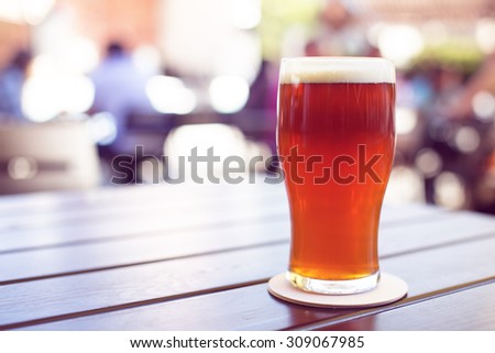 Pint of crafted ale on wooden table in beer garden