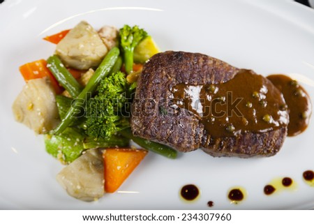 Main dish of grilled stake with black pepper sauce, garnished with green bean and carrot served in a white plate