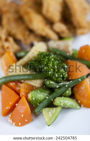Collection of steamed vegetables in a white plate with golden fried chicken in the background