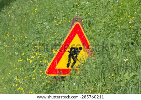 Men at work sign partially covered by a green grass field