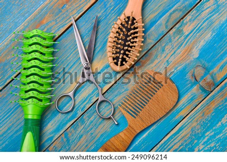 professional scissors for haircuts and two wooden combs color beech and plastic green lie on blue wooden table