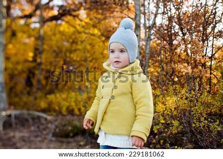 Very cute little girl in a yellow jacket in autumn