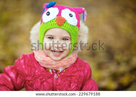 Smiling little girl in a red jacket and hat with owl