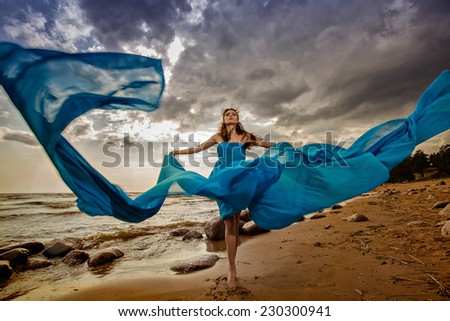 Beautiful slim girl in blue flowing dress on the sky background