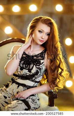 The girl with red hair in a black and white dress sitting on a chair on the background lights