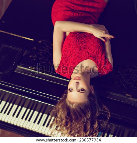 Girl in a red dress lying on the piano