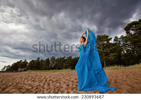 Slim sexy girl in blue flowing dress against the sky stands on the stone
