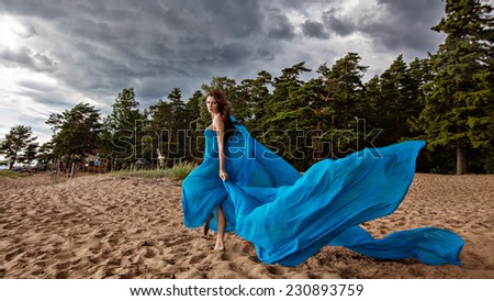 Beautiful sexy slim girl in blue flowing dress on the sky background