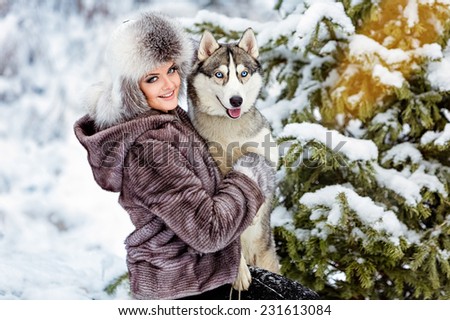 The girl in the gray coat smiling next to a grey husky dog in winter