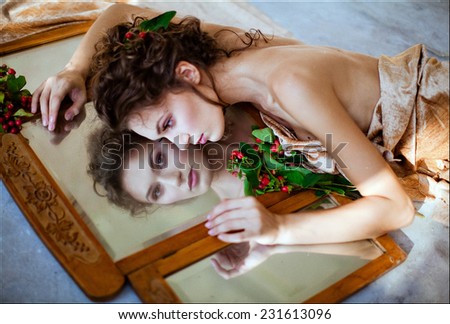 Curly sensual girl lying about a mirror, reflecting in it and near red berry