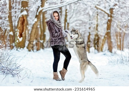 Cute girl keeps his paws dog husky on the background of the forest in winter