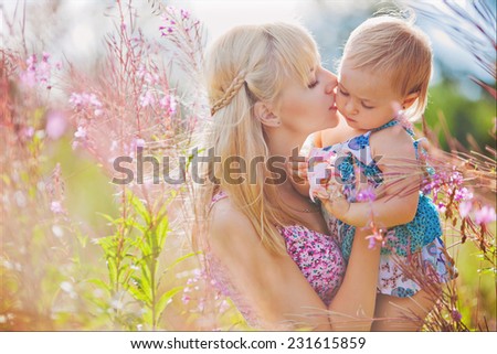 Mother gently kisses his daughter in a field on a background of flowers