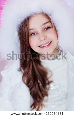 Cute long-haired young girl with blue eyes in a white hood with fur smiling, close up