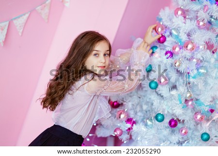 young curly girls with blue eyes with a white blouse hanging toys on the Christmas tree