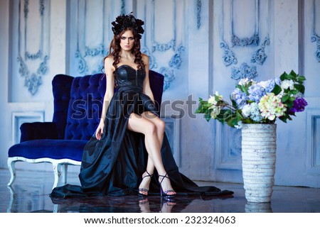 Long haired sensual brunette with a wreath of black flowers sitting on a blue sofa