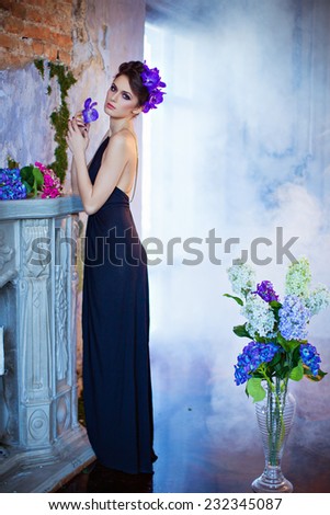 Beautiful slender brunette standing by the fireplace next to flowers