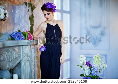 Beautiful slim brunette with eyes closed standing by the fireplace next to flowers