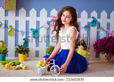 Very cute curly haired young girl in a blue skirt sitting on the floor and plays with Chicks for Easter