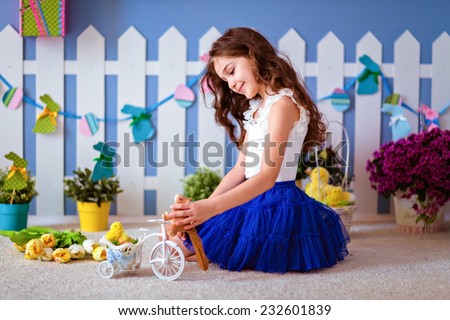 Very cute long-haired young girl in a blue skirt sitting on the floor and plays with Chicks for Easter