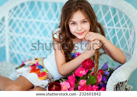 Very sweet smiling curly haired young girl sitting near the basket with flowers