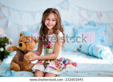 Very cute curly haired young girl sitting on the bed with soft toy