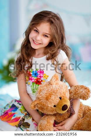 Very sweet smiling curly haired young girl sitting on the bed with soft toy