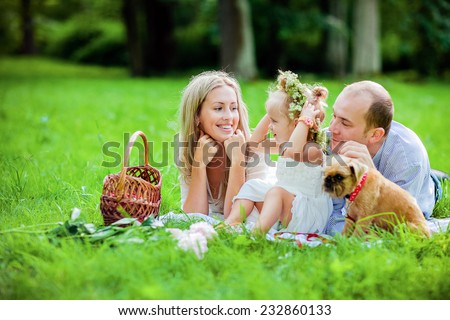 Mom, dad, little girl blonde and dog happy lie together on the grass