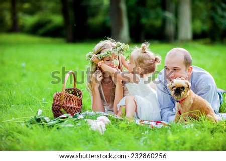 Mom, dad, little girl blonde and dog lie together on the grass and try on a wreath