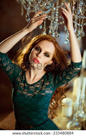 Red-haired curly girl in a green dress amid crystal chandeliers