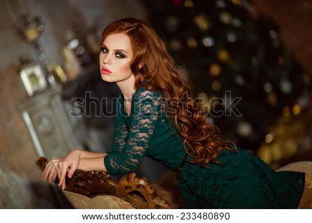 Beautiful red-haired curly girl in a green dress against the background of the Christmas tree