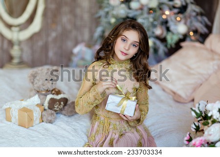 Charming long-haired young girl with blue eyes opens the gift on the Christmas tree background