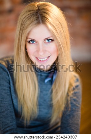 Glamorous blonde girl in the blue shirt smiling against a brick wall