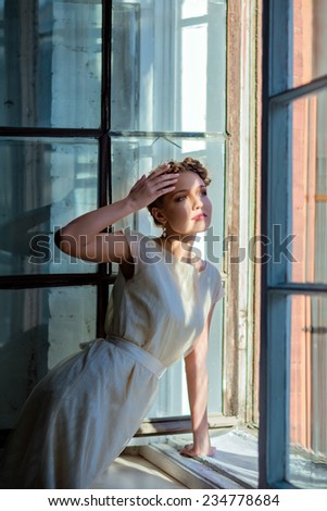 very beautiful sensual girl in a wedding dress looking out of the window