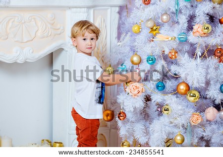 Small very cute blond boy hanging toys on a white Christmas tree