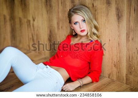Beautiful sexy blonde girl in a red blouse lying on the floor